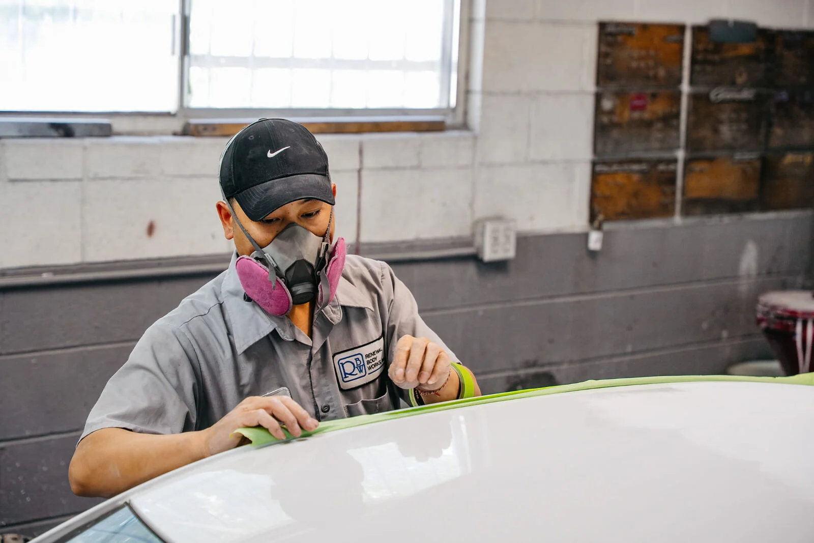 Technician applying fine-line masking tape to a white vehicle roof before painting