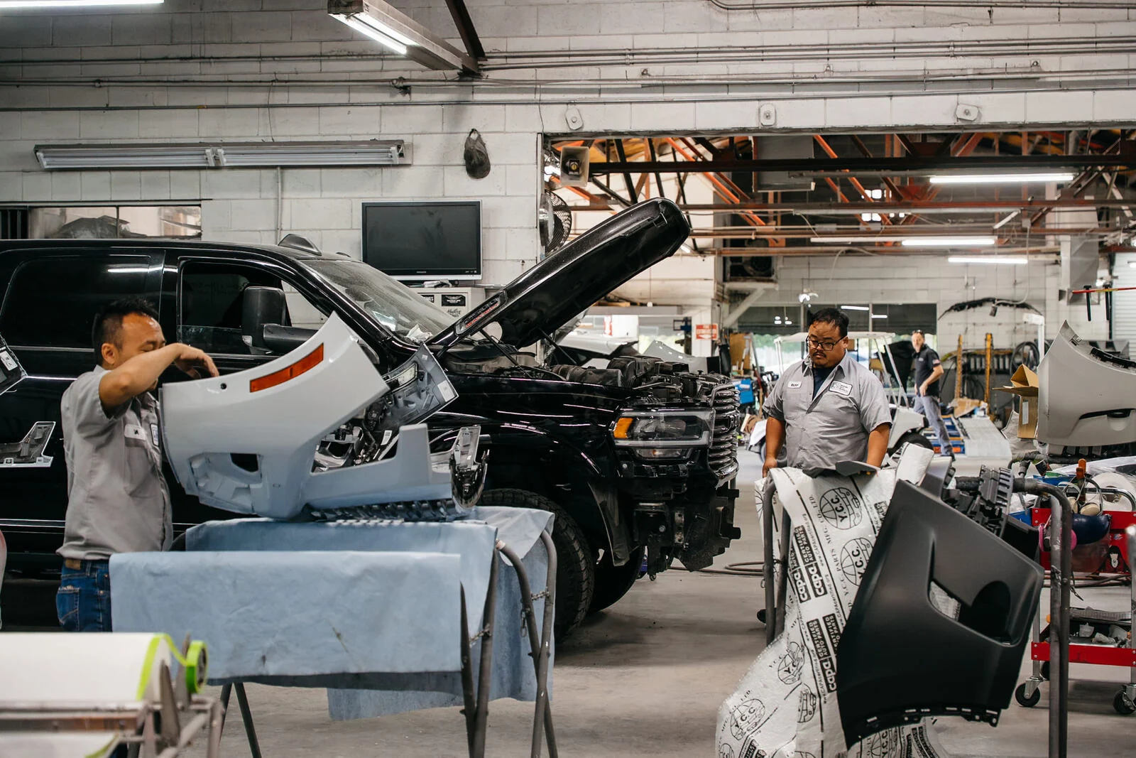 Two Renewal Body Works technicians preparing replacement parts beside a truck in the repair bay